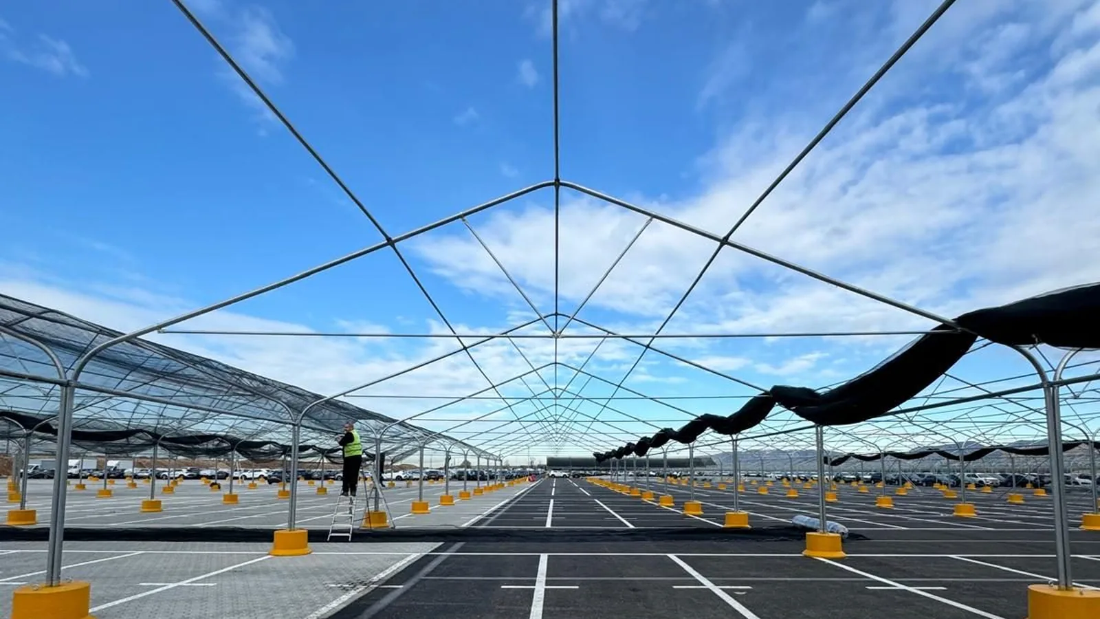 Struttura Hail Net Euromet con arcate in acciaio zincato su un grande parcheggio aziendale con centinaia di veicoli in sosta