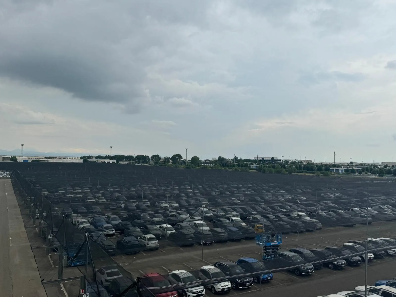 Piazzale di concessionaria con auto nuove parcheggiate sotto una copertura modulare in acciaio zincato con rete antigrandine